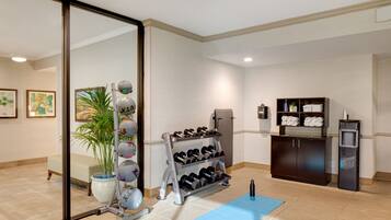 A clean, well-lit room with a massage chair, a wall-mounted shoe rack, a water dispenser, and a blue exercise mat.