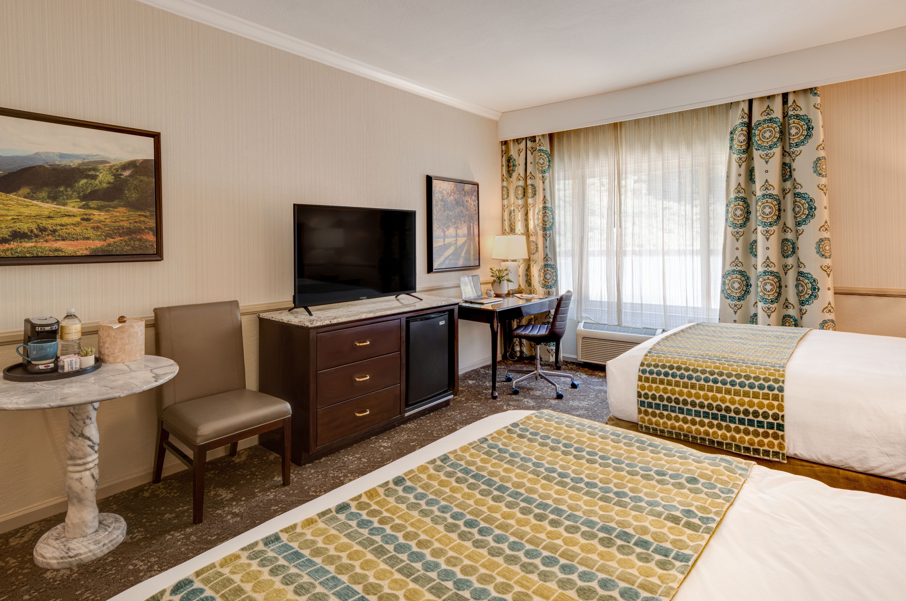 A hotel room with a bed, a desk with a computer, a television, and a small table with a lamp.
