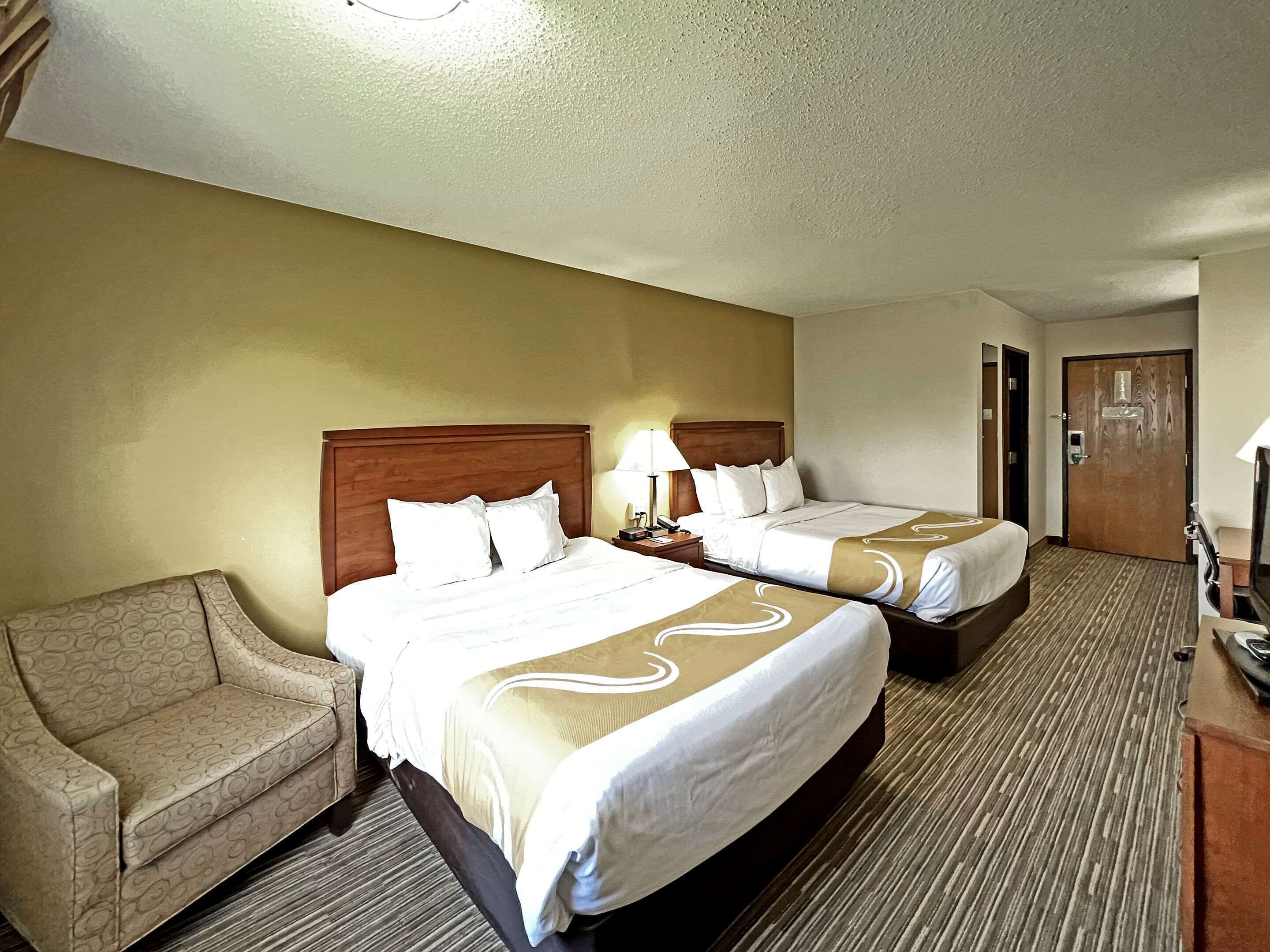 A hotel room with two beds, a sofa, a desk, and a door.