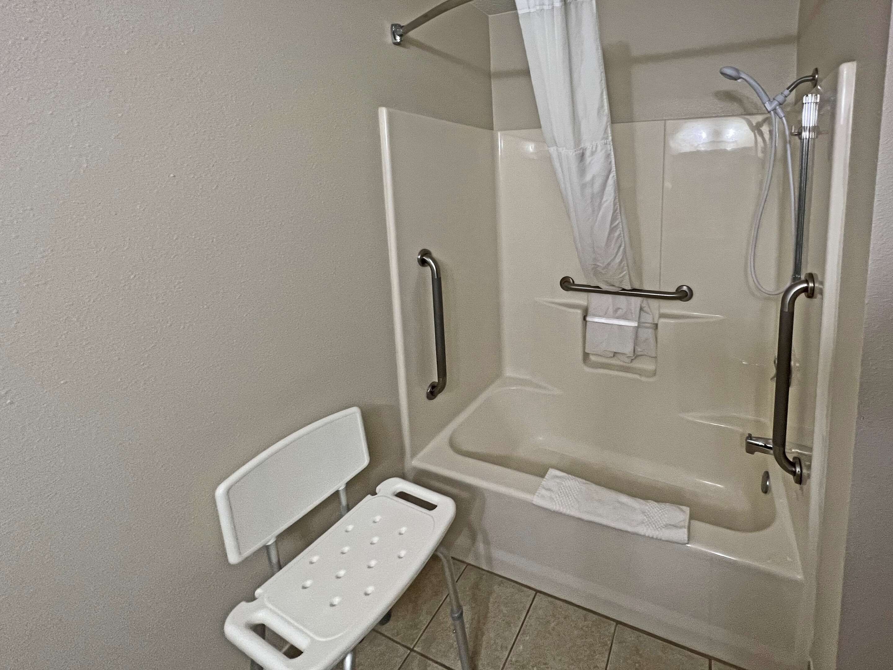 A shower area with a grab bar, a bench, and a handheld showerhead.