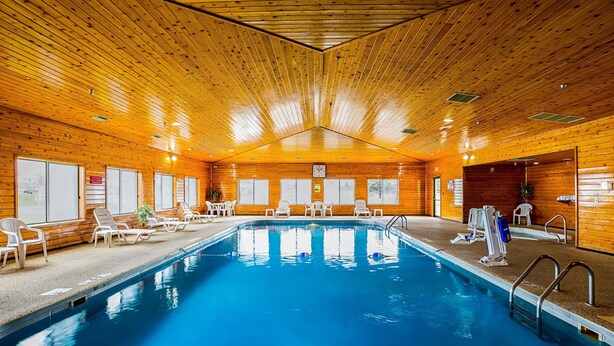 Una piscina interior con paredes y techo de madera, rodeada de sillas de descanso y un puesto de socorrista.