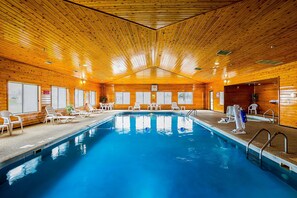 Una piscina interior con paredes y techo de madera, rodeada de sillas de descanso y un puesto de socorrista.