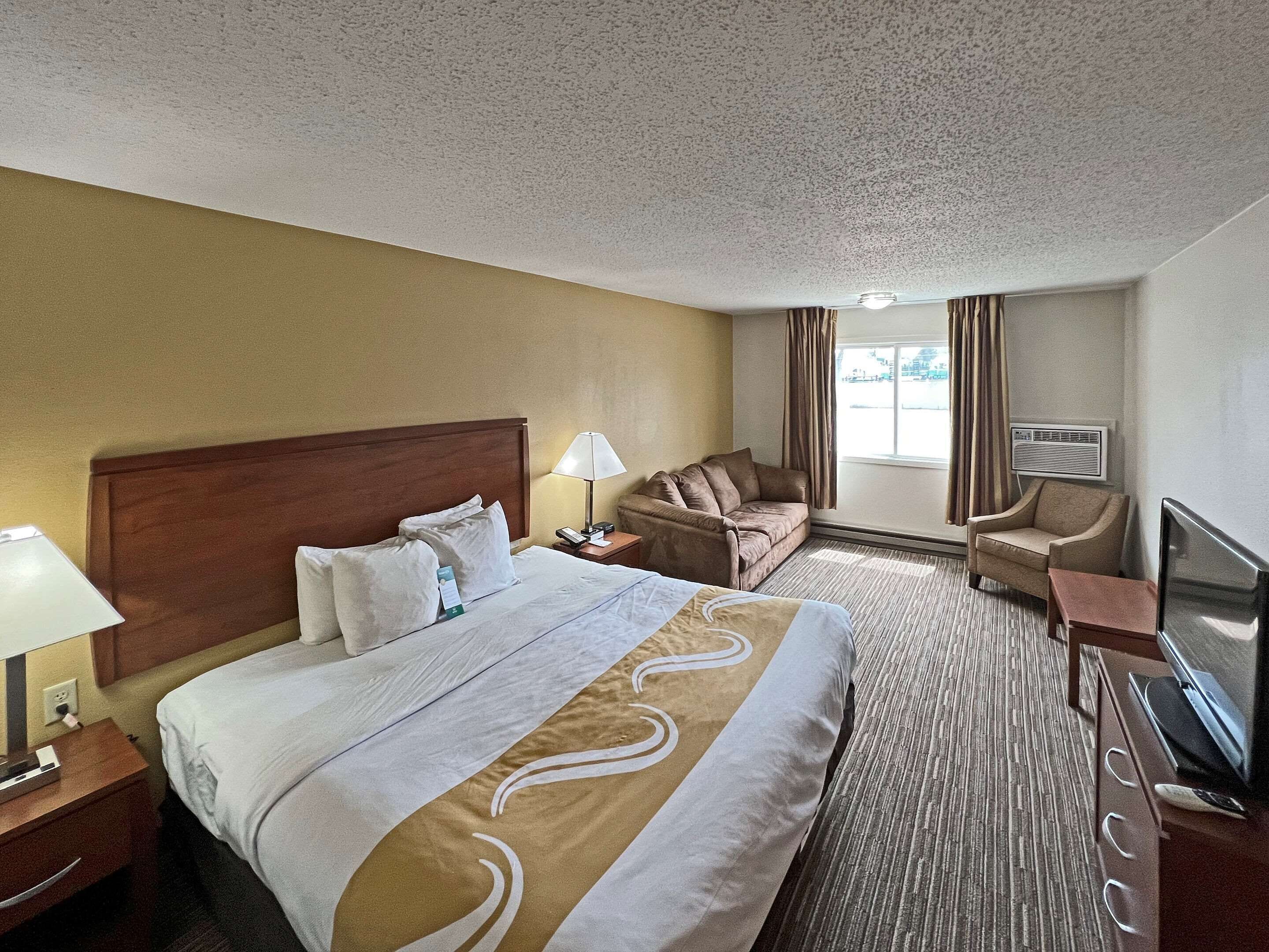 A hotel room with a large bed, a sofa, a chair, a TV, and a window with curtains.