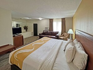 A hotel room with a large bed, a desk with a television, a leather sofa, and a lamp.