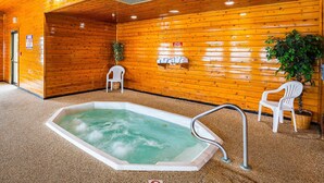Un interior de madera con una bañera de hidromasaje, dos sillas de plástico blanco y una planta en maceta.
