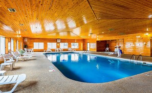 An indoor swimming pool with wooden walls and ceiling, surrounded by white lounge chairs and a lifeguard stand.