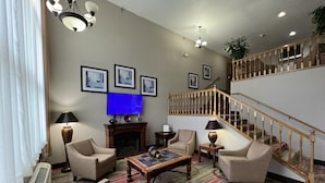 Amplia sala de estar con chimenea, asientos cómodos, televisor de pantalla plana y escalera con barandilla de madera.