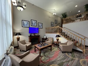 Cozy living room with a fireplace, comfortable seating, and a TV. A staircase leads to an upper level with framed pictures on the walls.