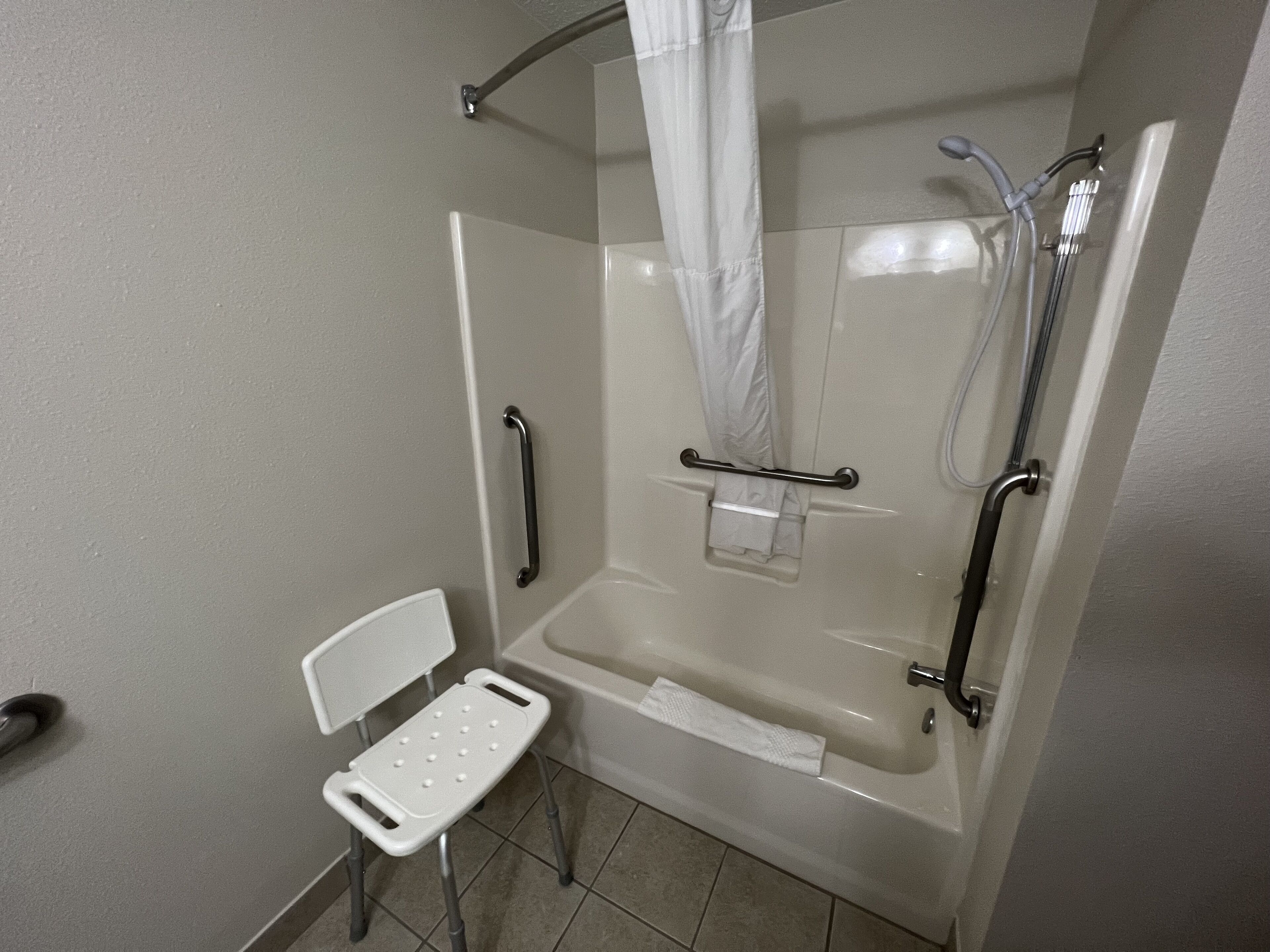 Une douche équipée d’une barre d’appui, une chaise blanche et un porte-serviettes.