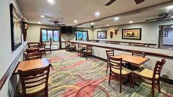 A restaurant with wooden tables and chairs, a patterned carpet, ceiling fans, and artwork on the walls.
