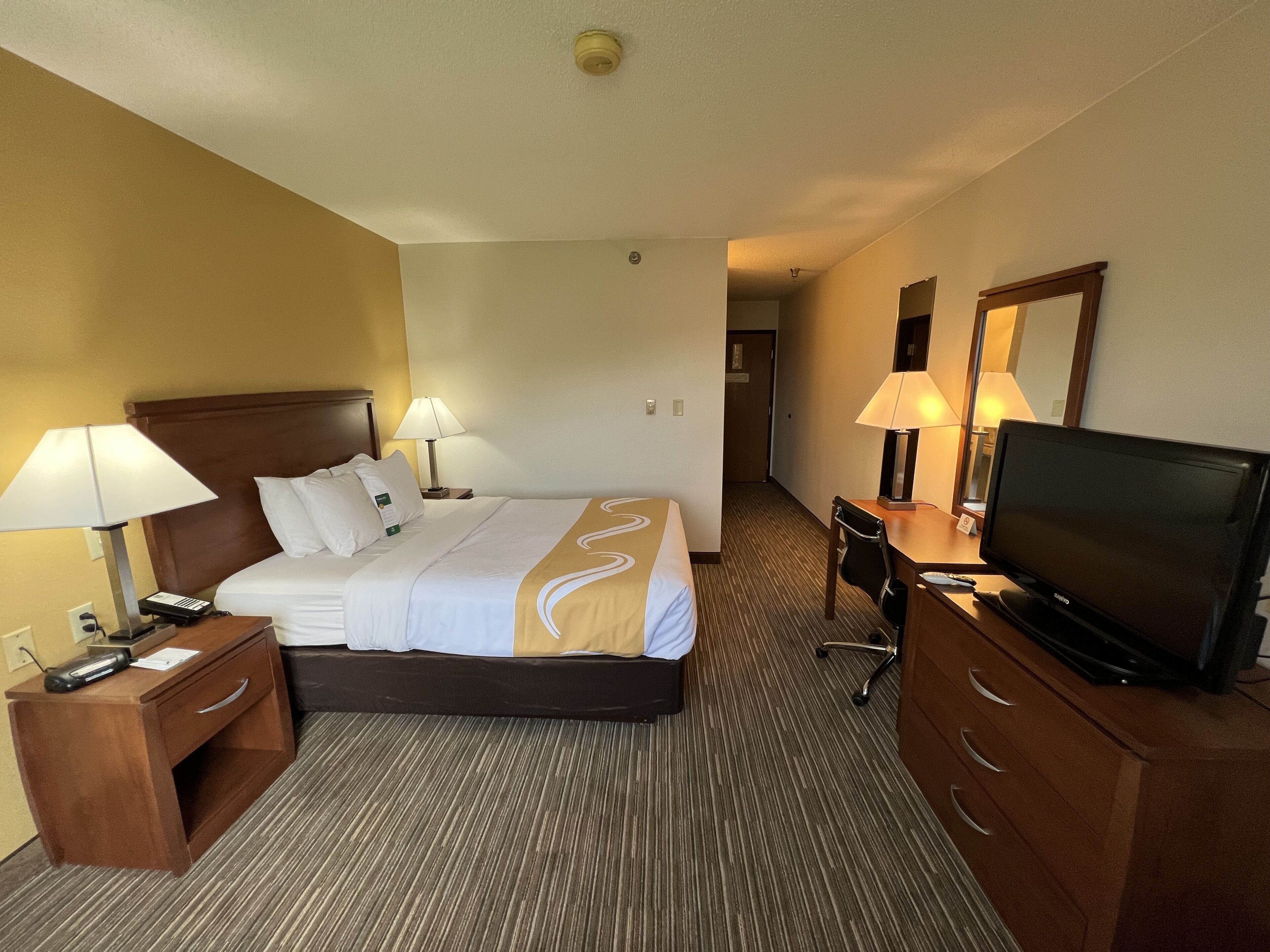 Ett hotellrum med en säng, sänglampor, ett skrivbord med en tv och en stol.