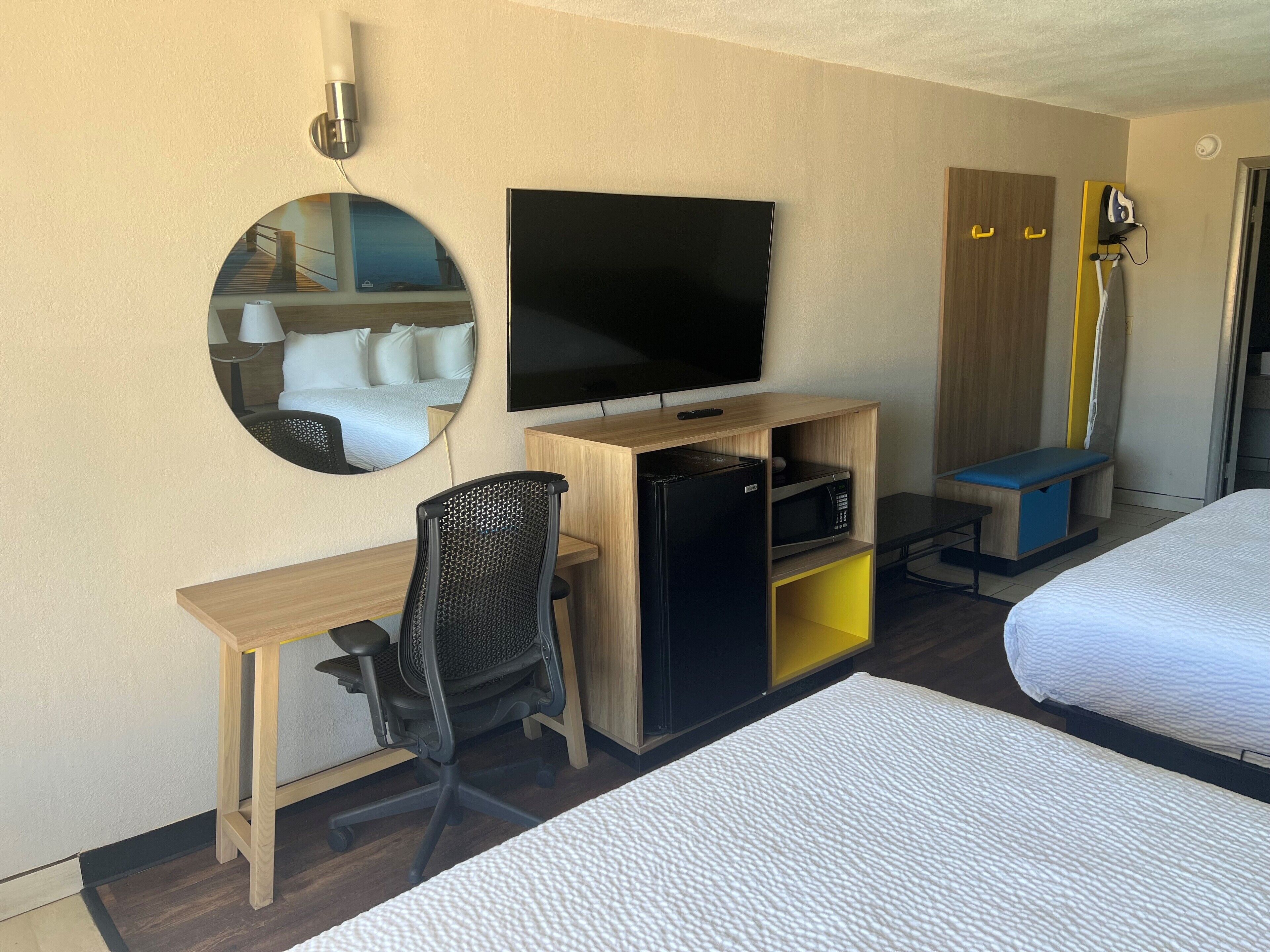 Ein Hotelzimmer mit Bett, Schreibtisch mit Stuhl, Fernseher, Kleiderschrank und Spiegel.