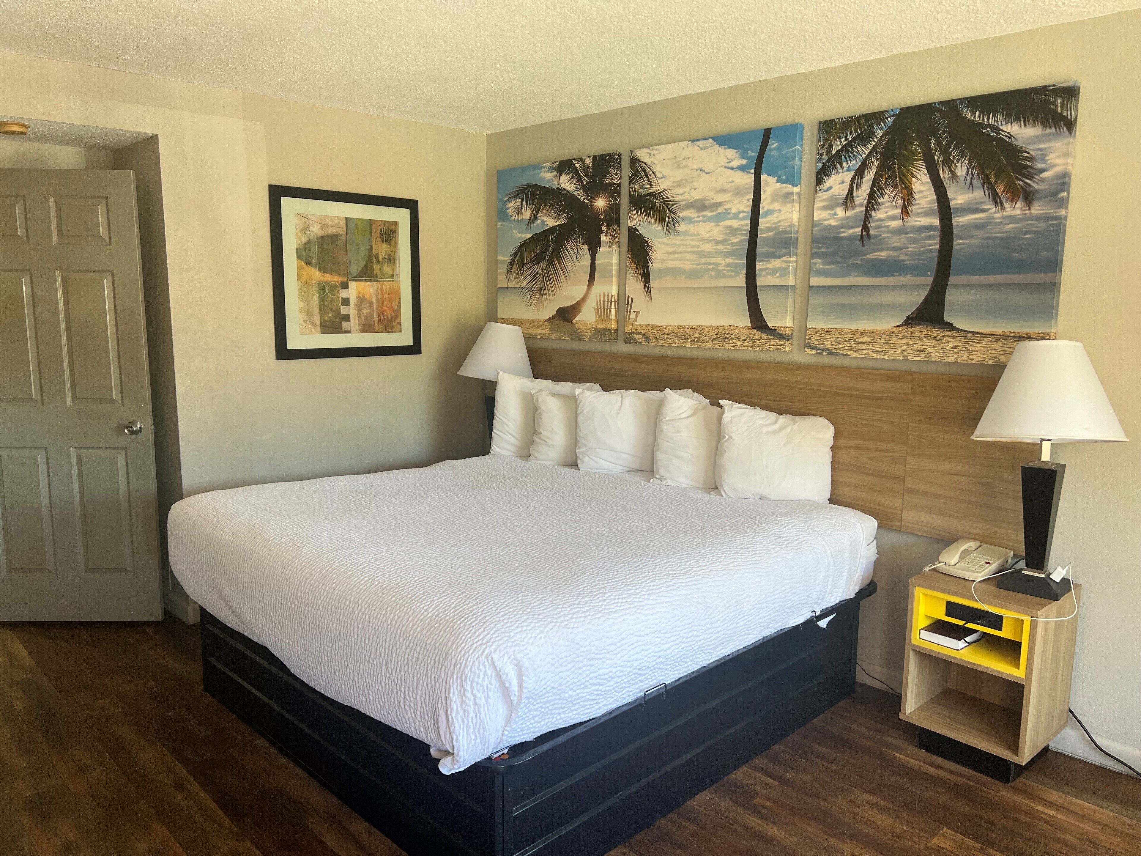 A neatly made bed with white bedding, a wooden headboard, and a nightstand with a lamp and phone.