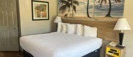 A neatly made bed with white bedding, a wooden headboard, and a nightstand with a lamp and phone.