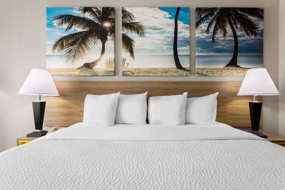 Ein Hotelzimmer mit einem großen Bett, zwei Nachttischlampen, einem hölzernen Kopfteil und Wandkunst zum Thema Strand.
