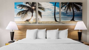 Een hotelkamer met een groot bed, twee bedlampjes, een houten hoofdeinde en een schilderij met een strandthema.