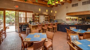 A restaurant with wooden tables and chairs, a bar area, and a view of the outdoors. - Inn on the Alameda (Santa Fe)