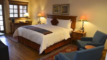 A neatly arranged bedroom with a large bed, two bedside tables with lamps, a chair, and a wooden headboard.