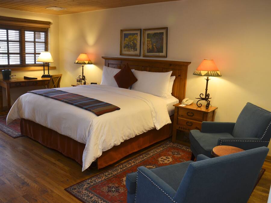 A neatly arranged bedroom with a large bed, two bedside tables with lamps, a chair, and a wooden headboard.