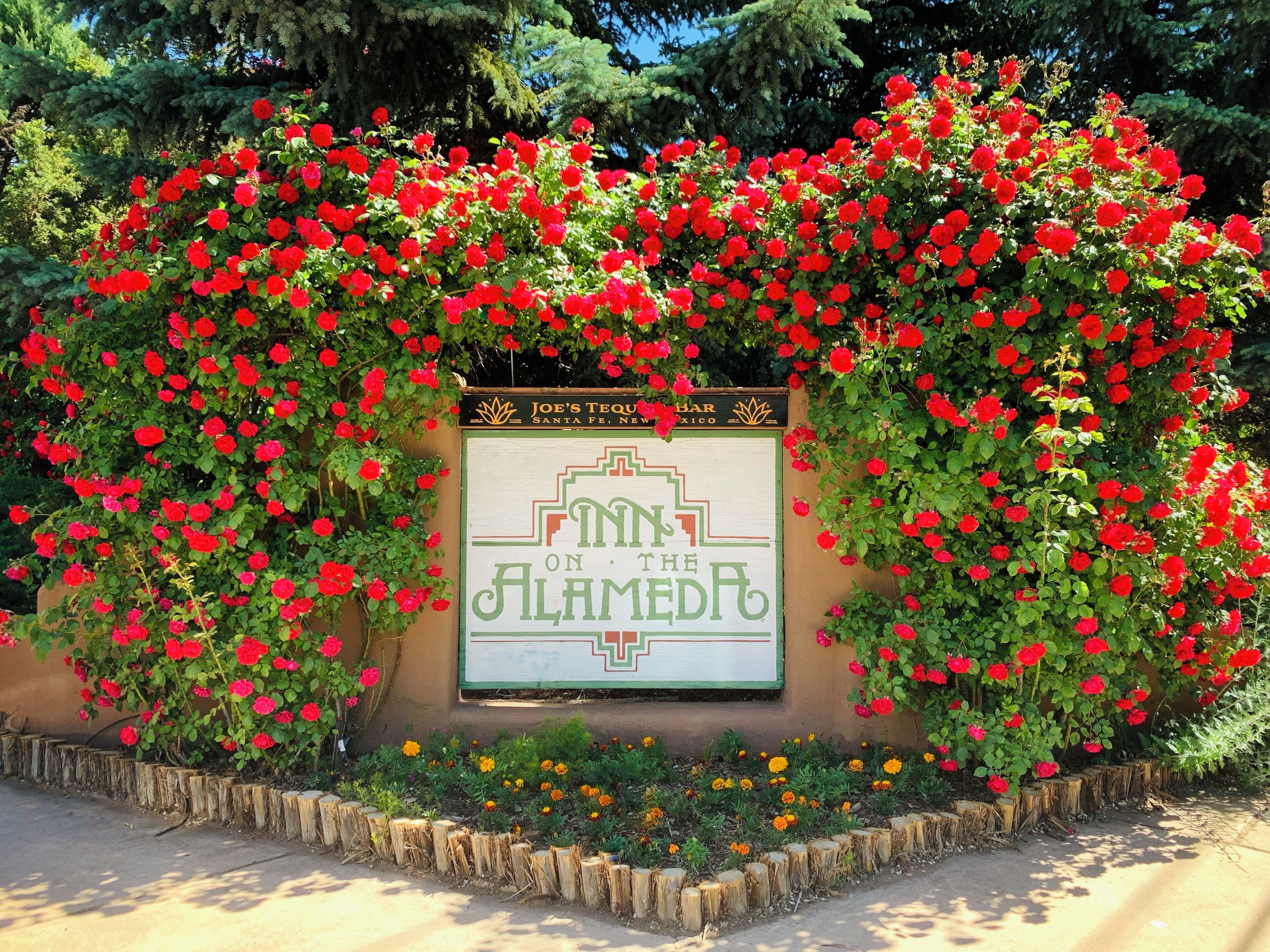 Letrero que dice 'Inn on the Alameda', rodeado de rosas rojas y caléndulas.