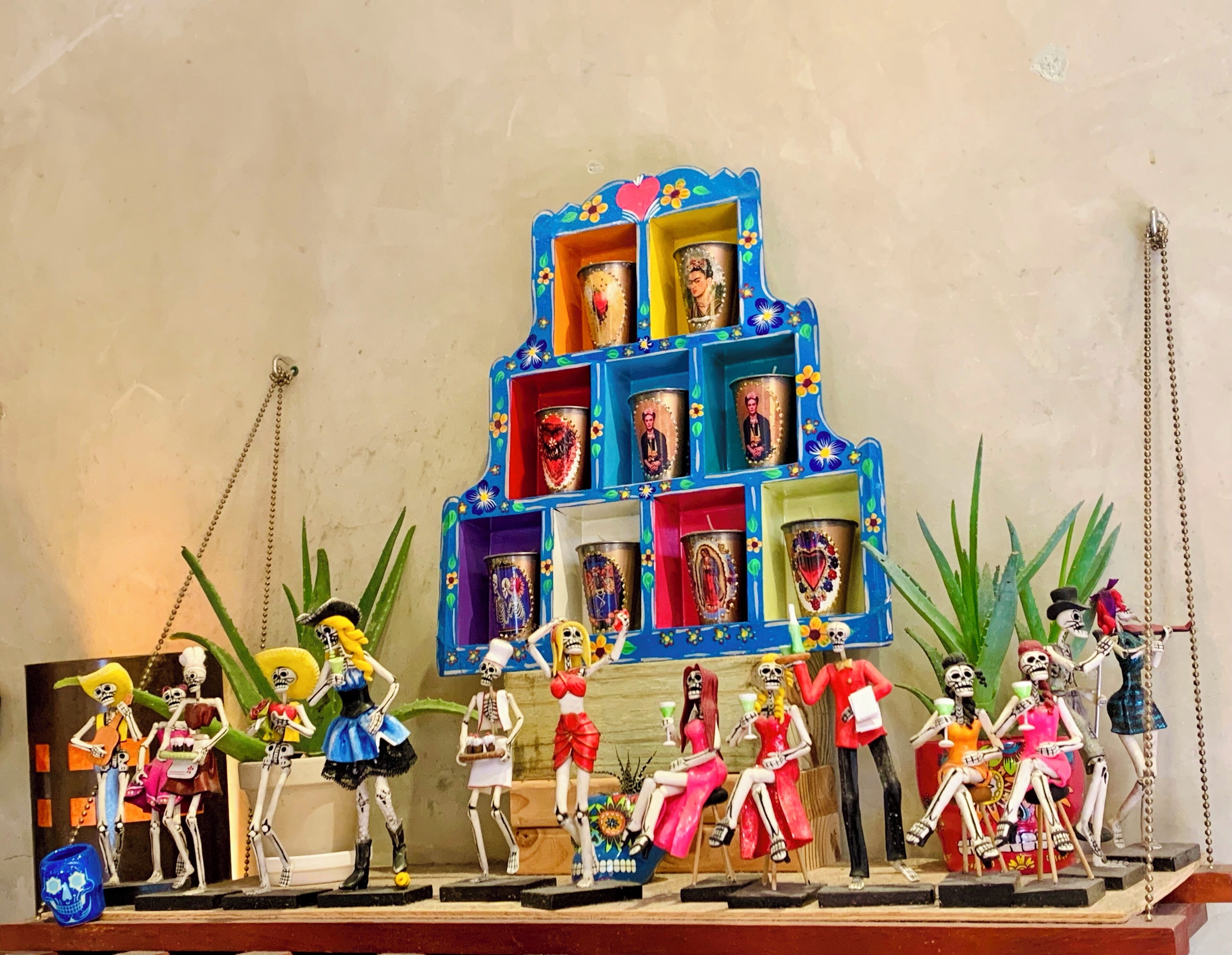 Una exhibición colorida de figuritas de esqueletos y un estante azul con fotografías.