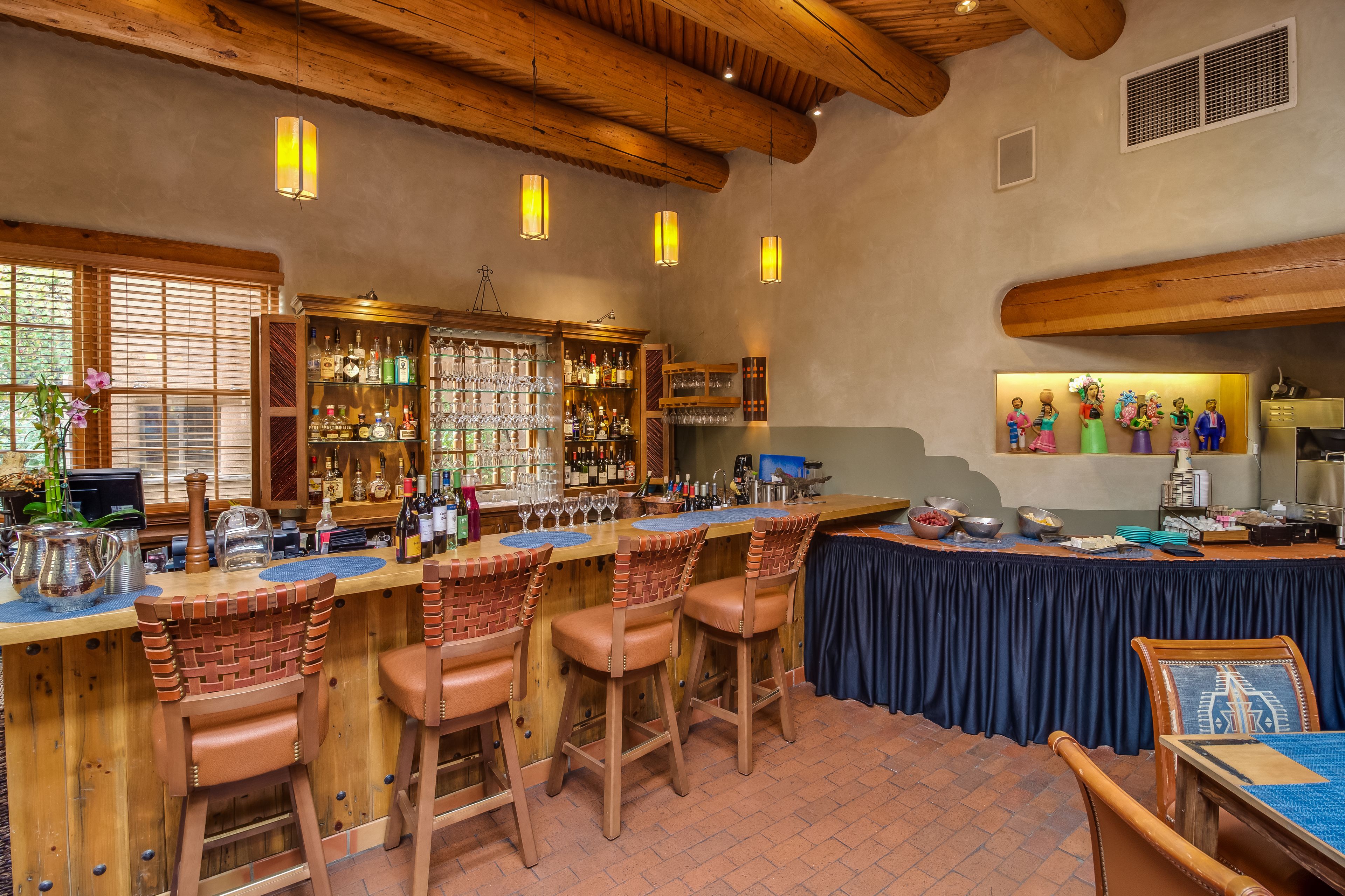 Zona de bar con taburetes de madera, una barra con botellas y vasos, y una pared decorada.
