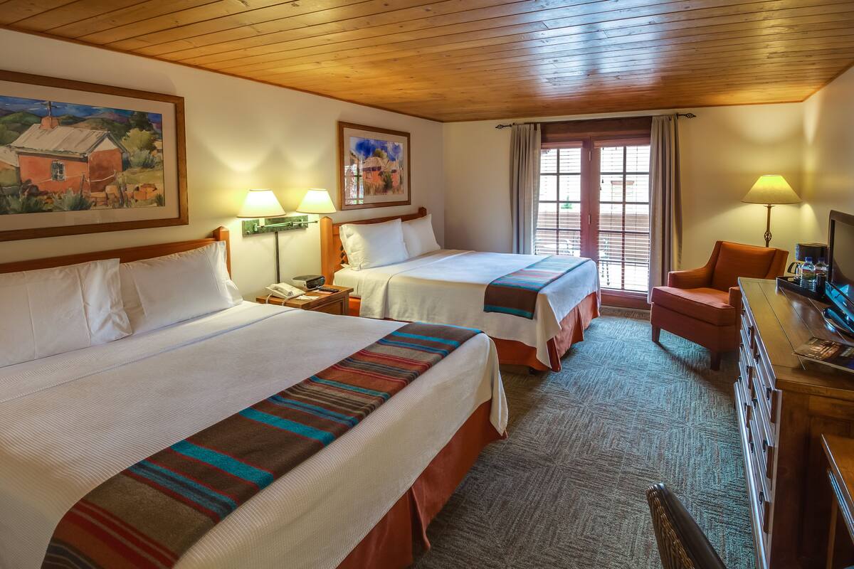 A hotel room with two beds, a desk, a chair, and a television.