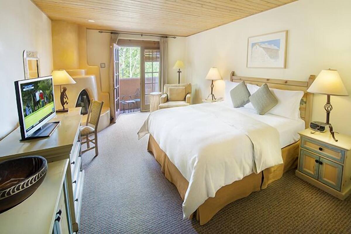 A hotel room with a bed, bedside tables, a desk with a computer, a chair, and a view of the outdoors.