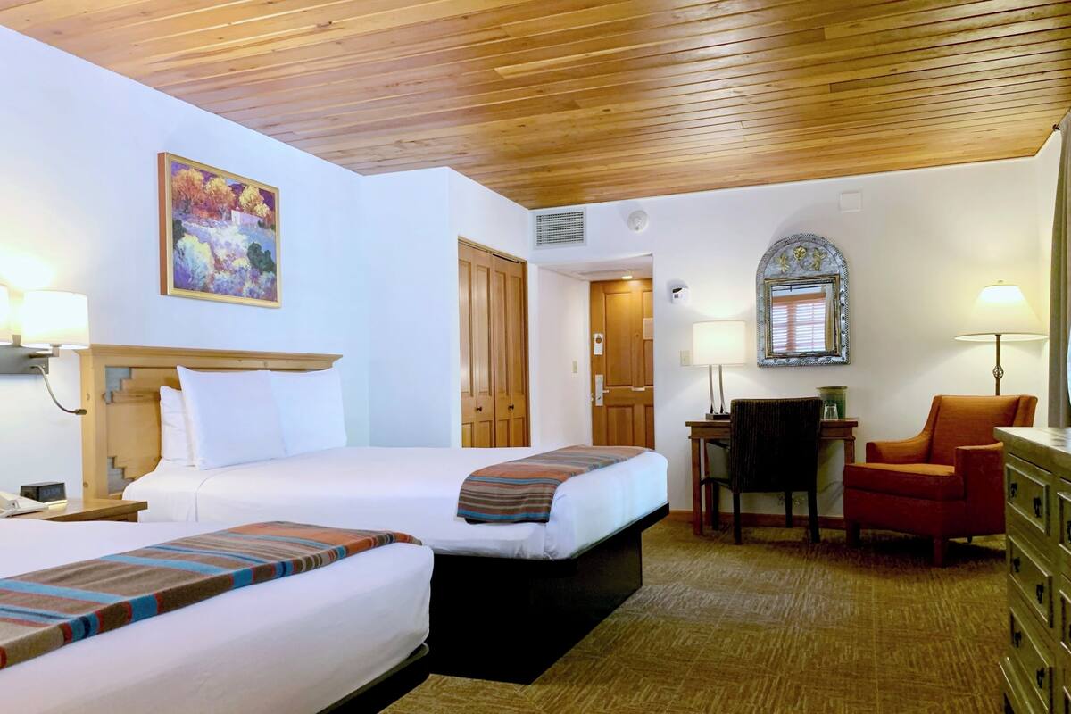 A hotel room with two beds, a desk, a chair, and a mirror.