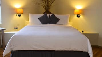 A neatly made bed with white and dark bedding, two wall-mounted lamps, and a vase with branches on the headboard.