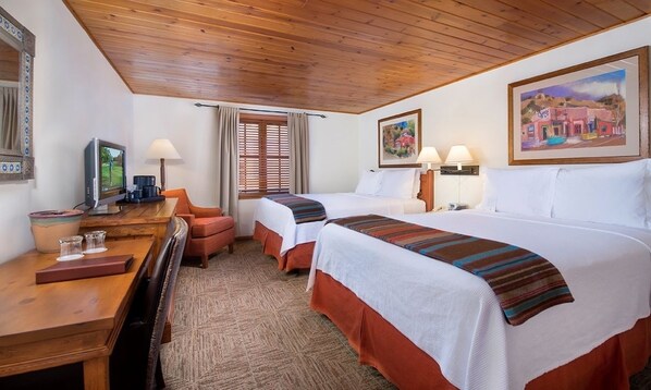A hotel room with two beds, a desk with a computer, a chair, and a window with curtains.