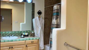 A bathroom with a wooden vanity, a shower with a striped curtain, a handrail, and a toilet paper holder.