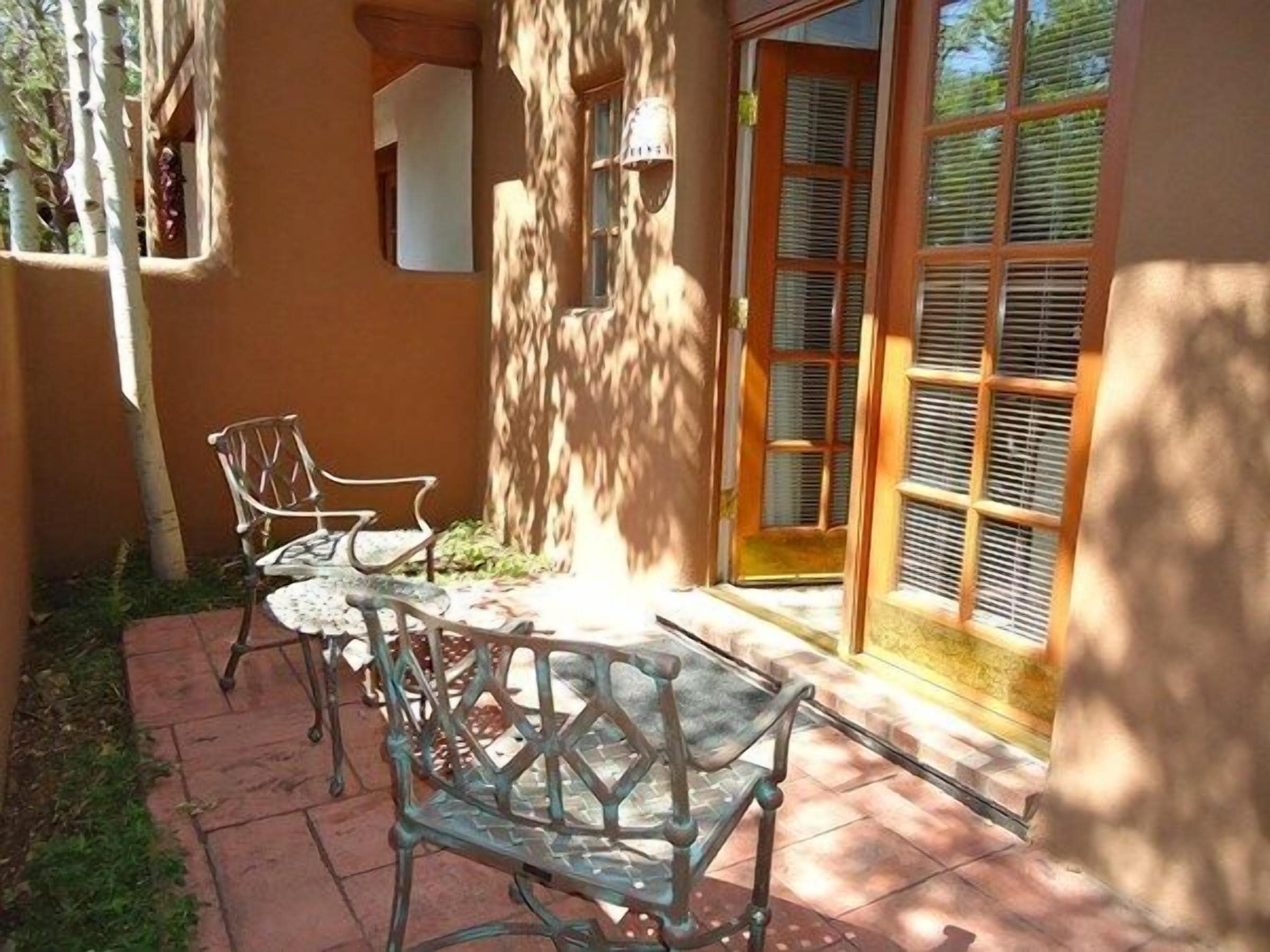 A patio with two metal chairs and a table, a wooden door with shutters, and a wall with a window.