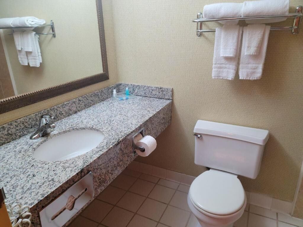 A bathroom with a granite sink, a toilet, and a towel rack with folded towels.