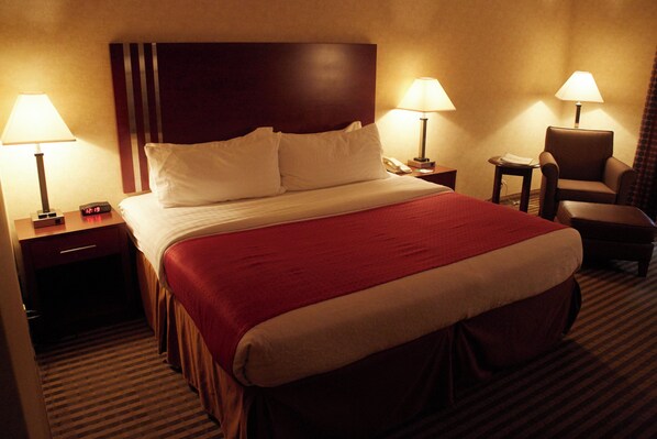 A hotel room with a large bed, two bedside tables, a chair, and two lamps.