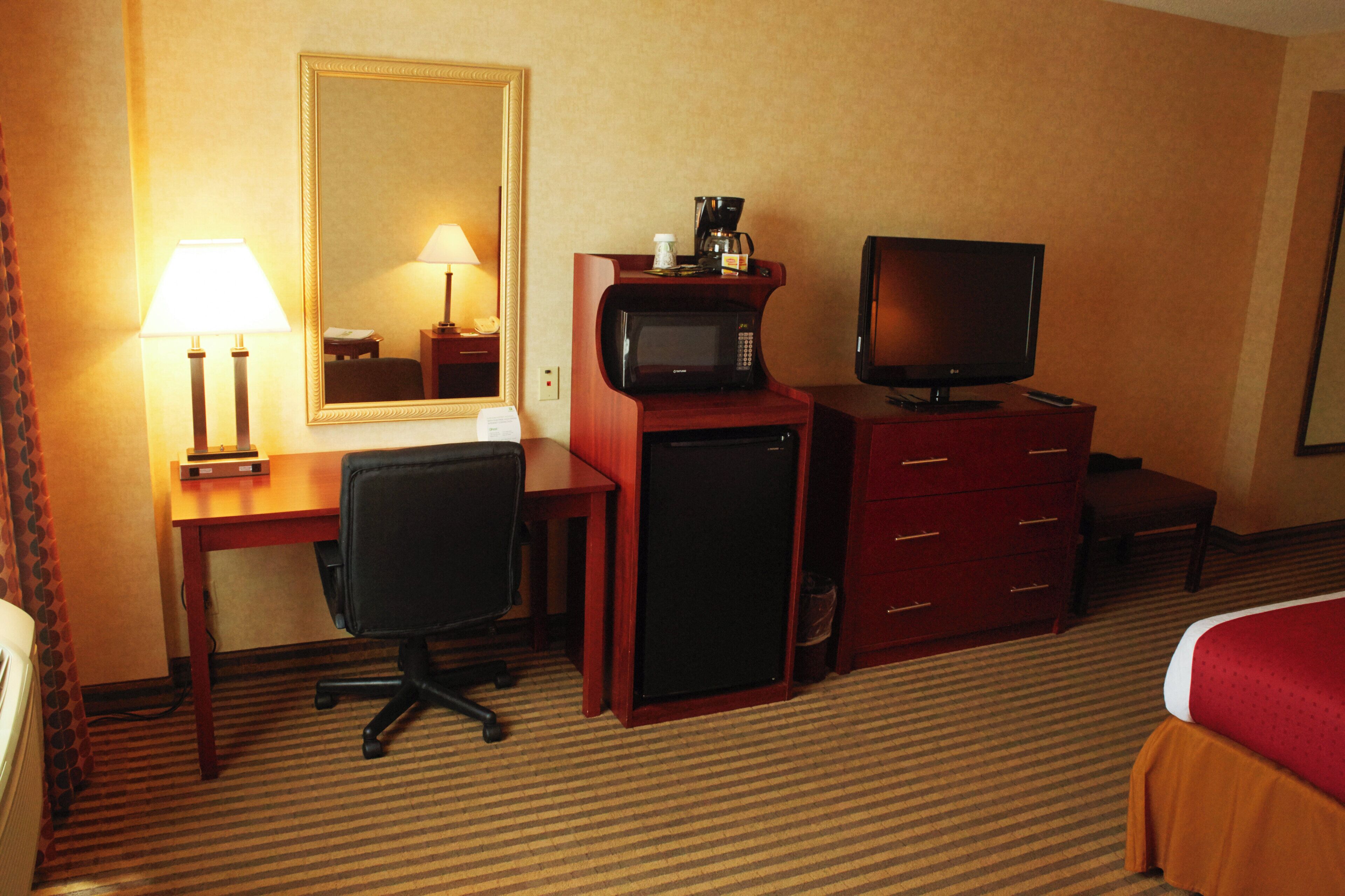 Een hotelkamer met een bureau, een stoel, een televisie, een magnetron en een bed.