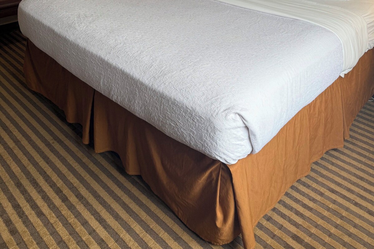 Une chambre d’hôtel avec un grand lit, une table de chevet, une lampe et un tableau encadré au mur.