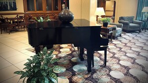 A grand piano in a spacious room with a patterned floor, wooden furniture, and a large window. - Lynchburg Grand Essential (Lynchburg)