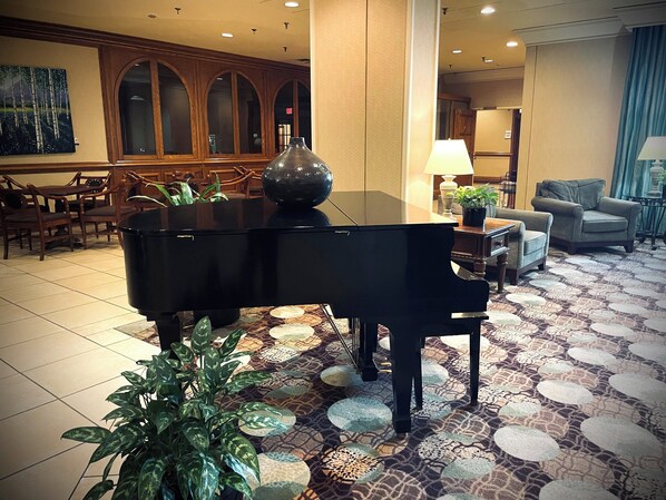 Un piano à queue se trouve dans une pièce spacieuse, dotée d’un parquet à motifs, de meubles en bois et d’une grande fenêtre.