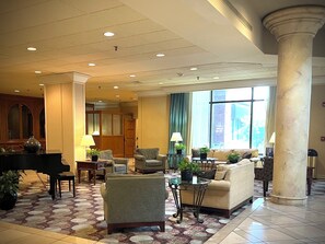 A lobby with a grand piano, multiple seating areas, a patterned carpet, and large windows.