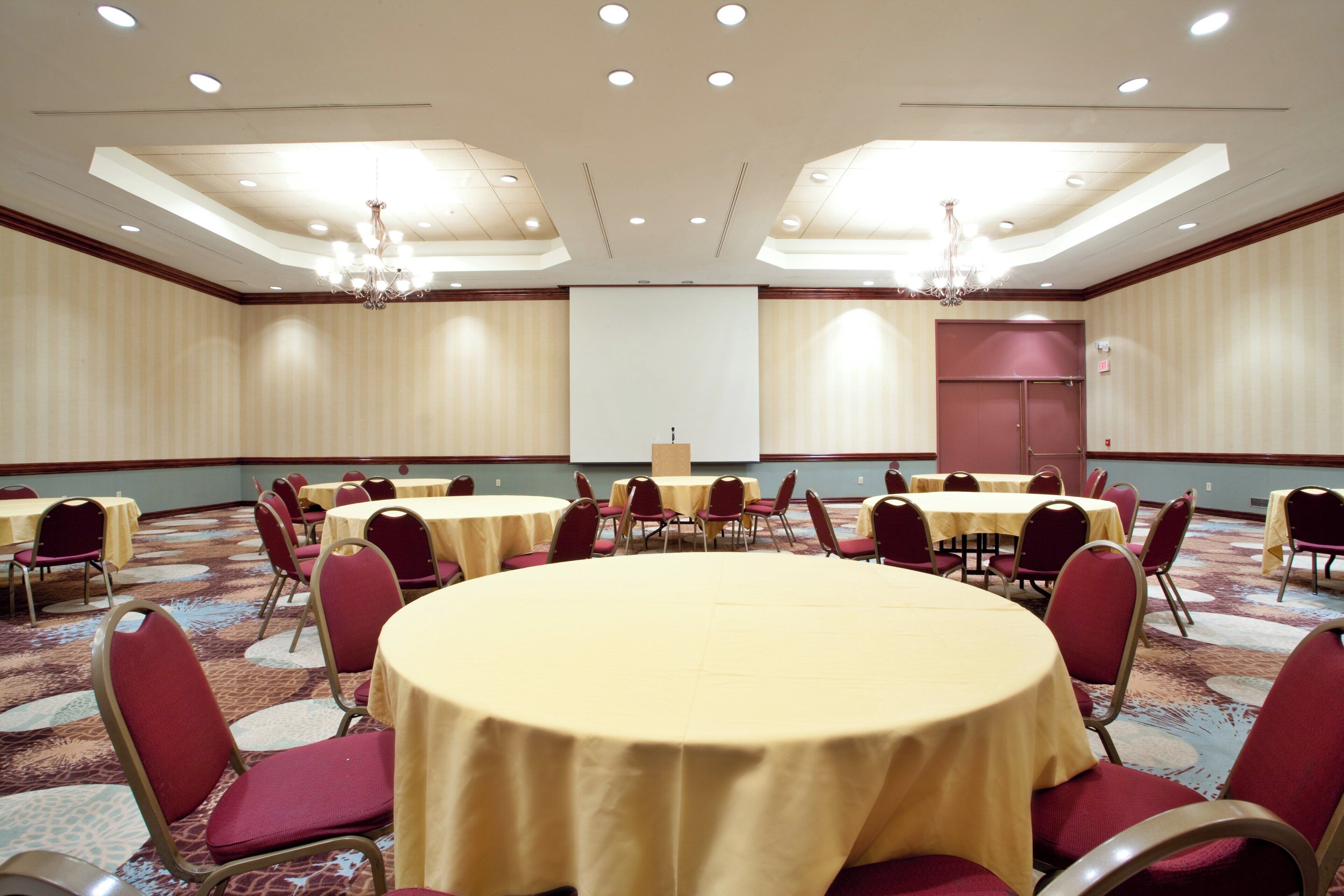 A conference room with round tables and chairs, a projector screen, and a large screen at the front.