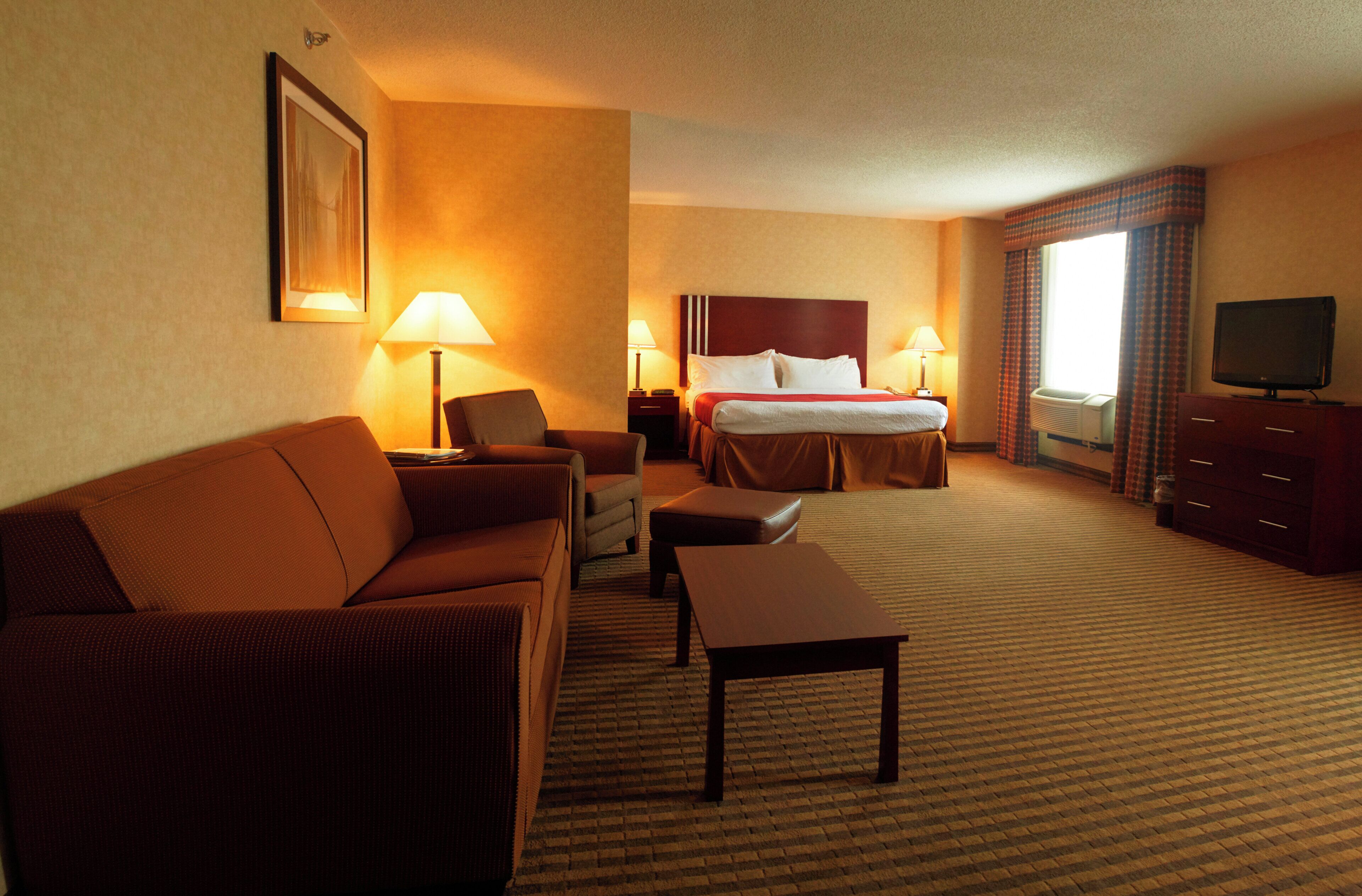 A hotel room with a bed, a sofa, a chair, a table, and a television.