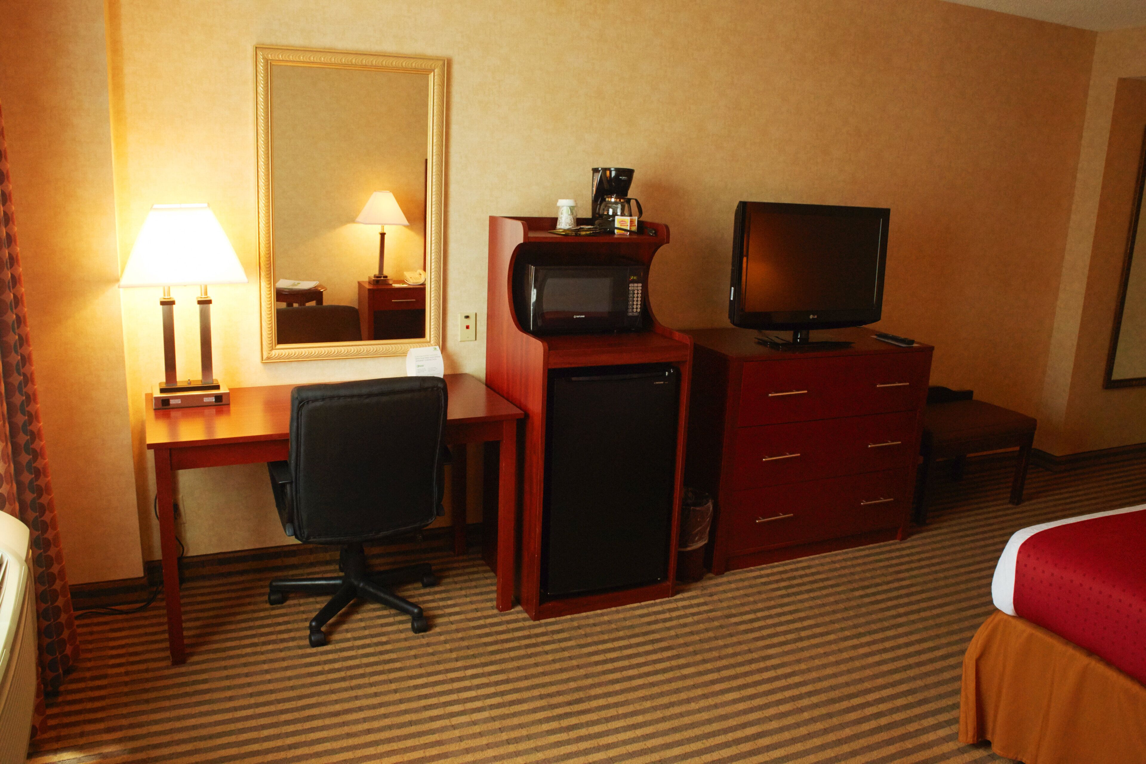 Une chambre d’hôtel équipée d’un bureau, d’une chaise, d’une télévision, d’un four à micro-ondes et d’un lit.