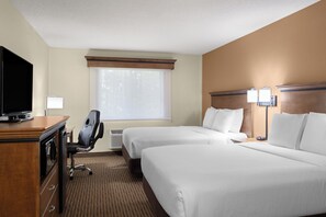 A hotel room with two beds, a desk with a television, a chair, and a window with blinds.