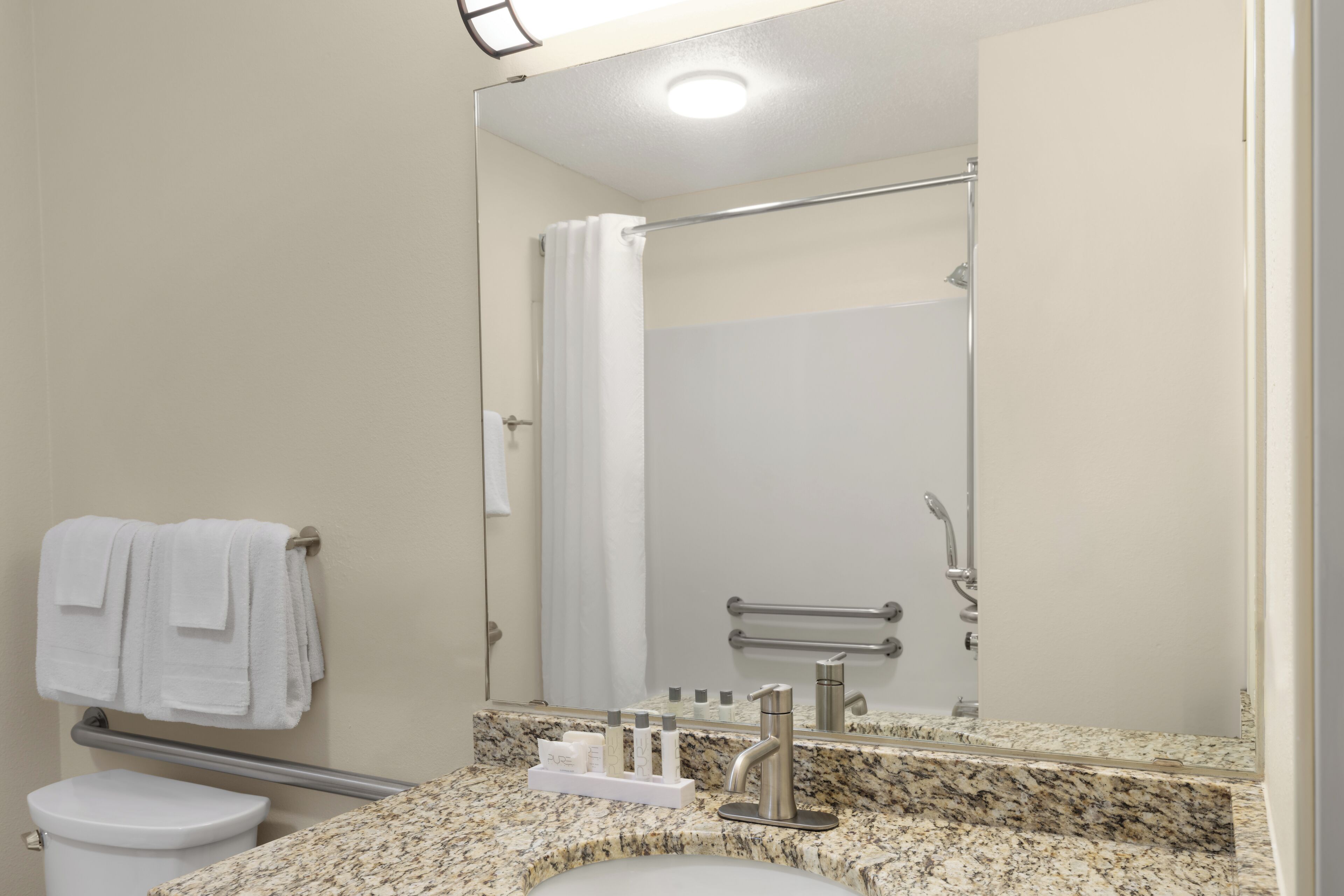 A bathroom with a toilet, a sink with a granite countertop, a mirror, and a shower area.