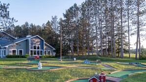 Un parcours de mini-golf avec un petit bâtiment rouge servant de club-house, entouré d’une pelouse et de grands arbres.