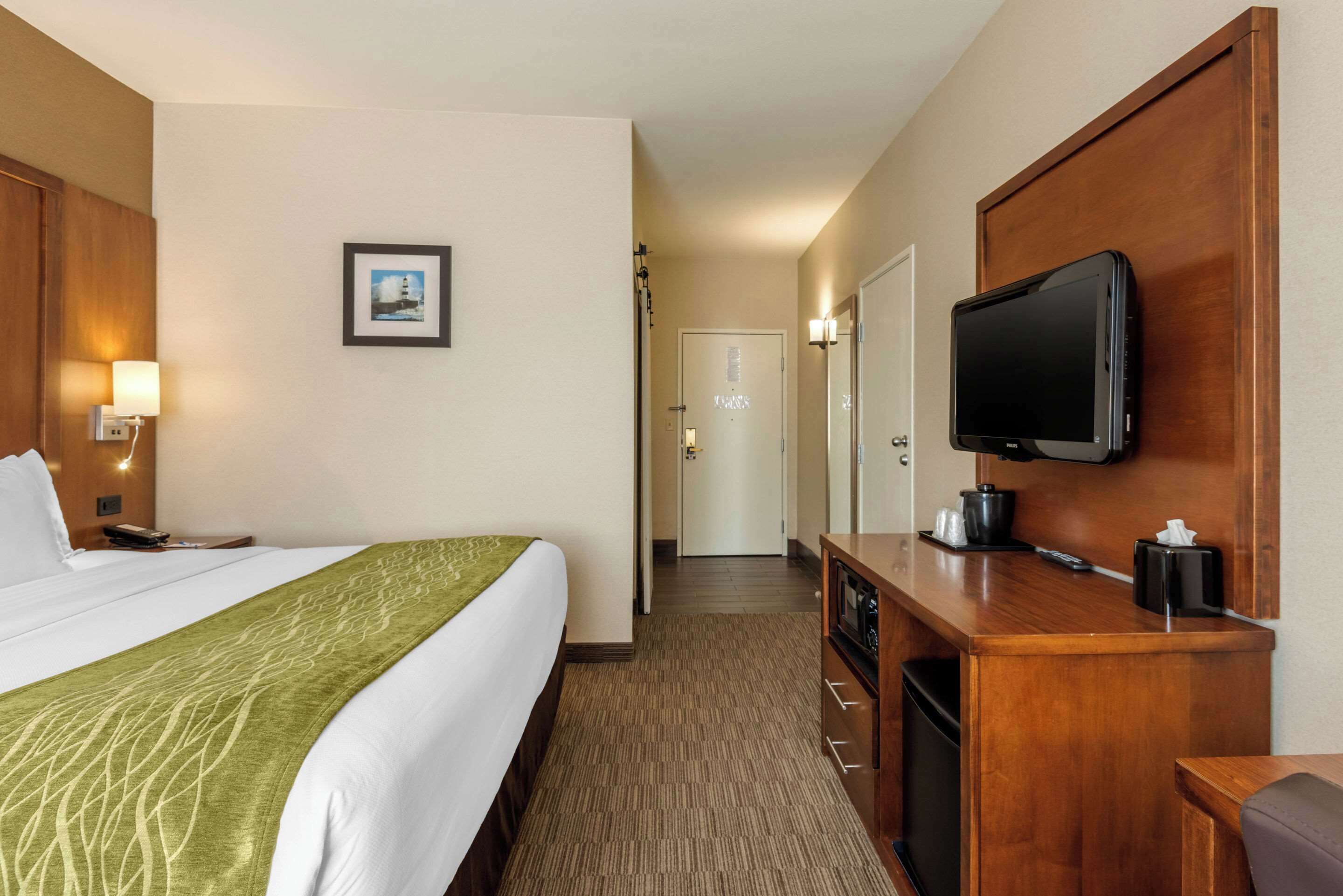 A hotel room with a bed, a television, a desk with a coffee maker, and a framed picture on the wall.