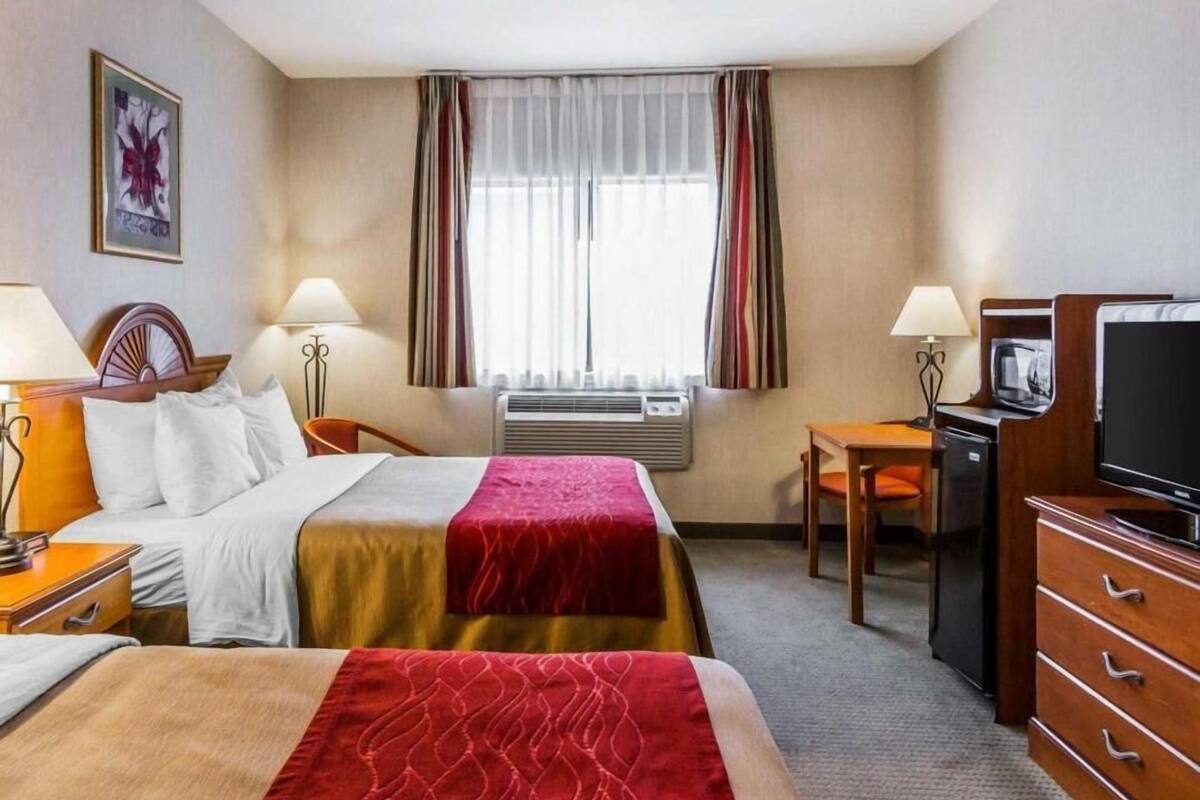 A hotel room with two beds, a desk, a television, and a window with curtains.