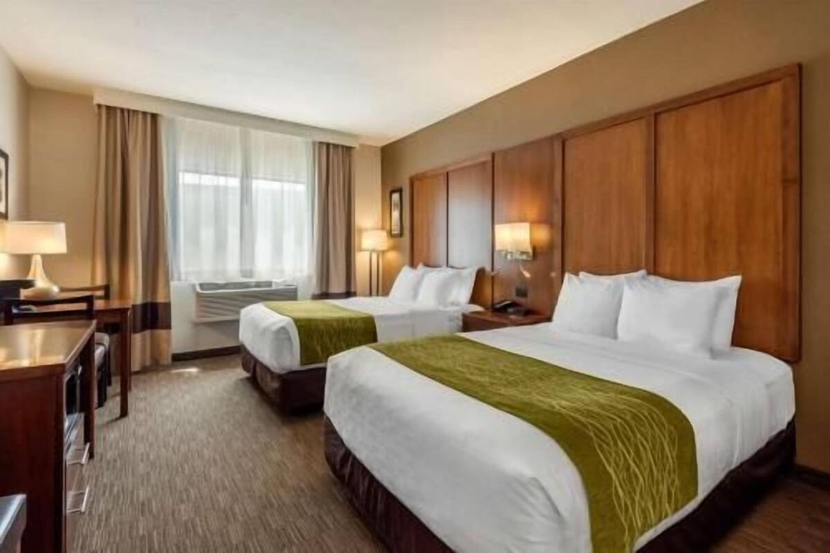 A hotel room with two beds, a desk, a chair, a lamp, and a window with curtains.