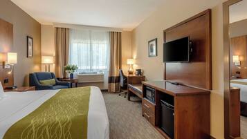 A hotel room with a large bed, a desk, a television, and a mirror.